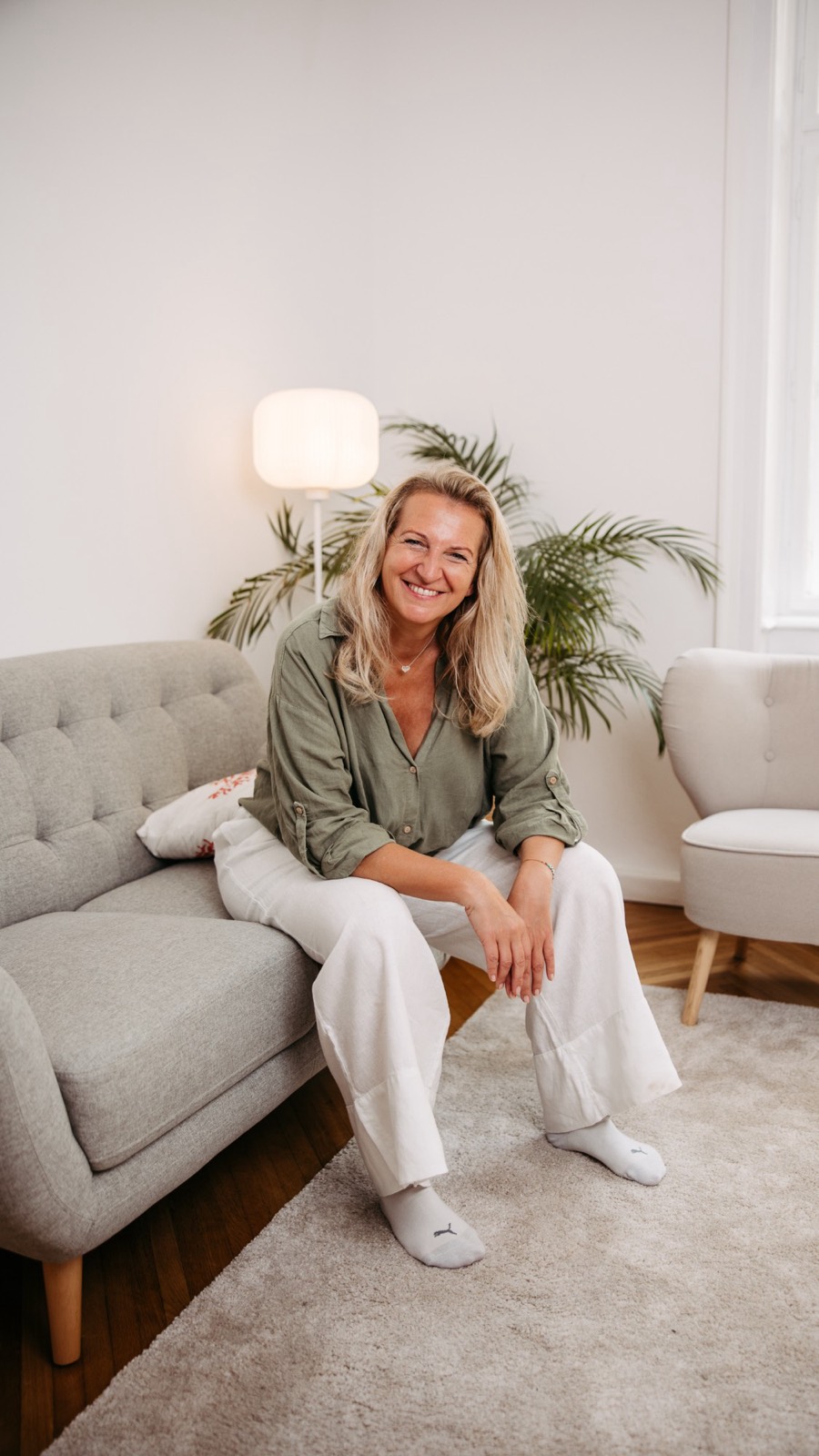 Maria Peischl lachend auf einem hellen Sofa